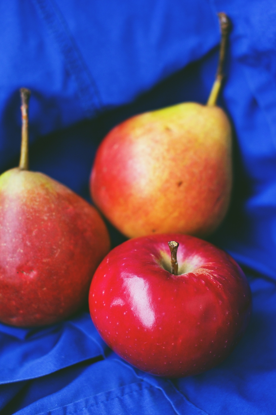 蓝色桌布上红苹果和梨水果摄影