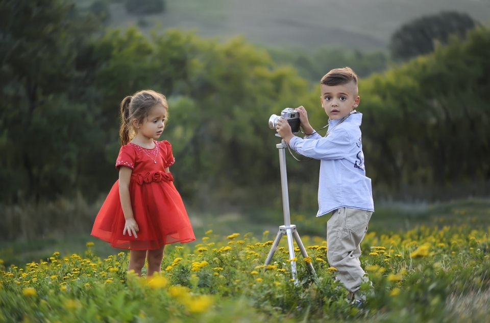 帅气小男孩在花丛中为红色连衣裙可爱小女孩拍照