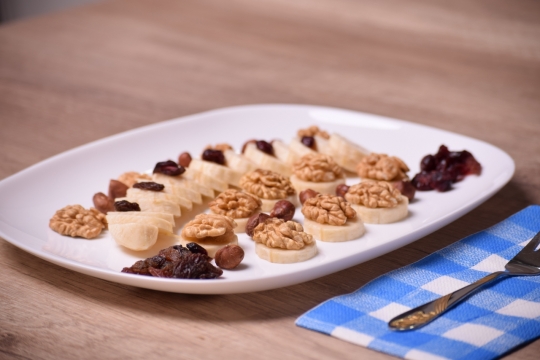 木桌格子布上叉子旁白色盘子放坚果