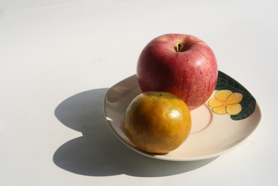 阳光下花纹盘子里的苹果和橘子水果