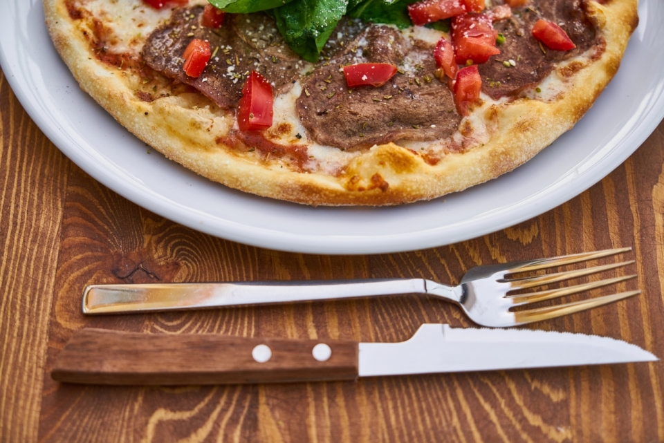 木桌盘子里的美味披萨和刀叉餐具摄影