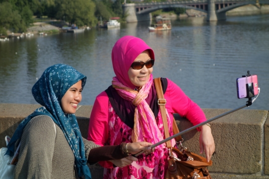 阳光下河流石桥上拿手机自拍的妇女