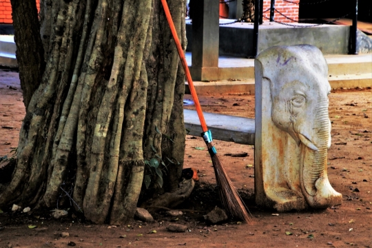 树根旁倚靠扫帚的白象石雕