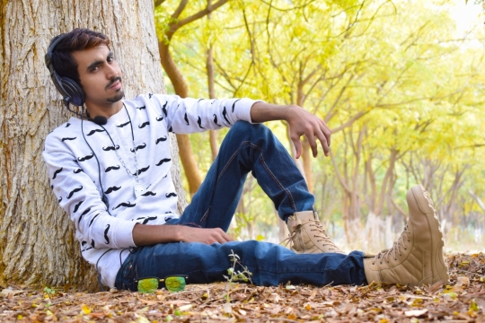 靠坐在大树底下头戴耳机的帅气男子