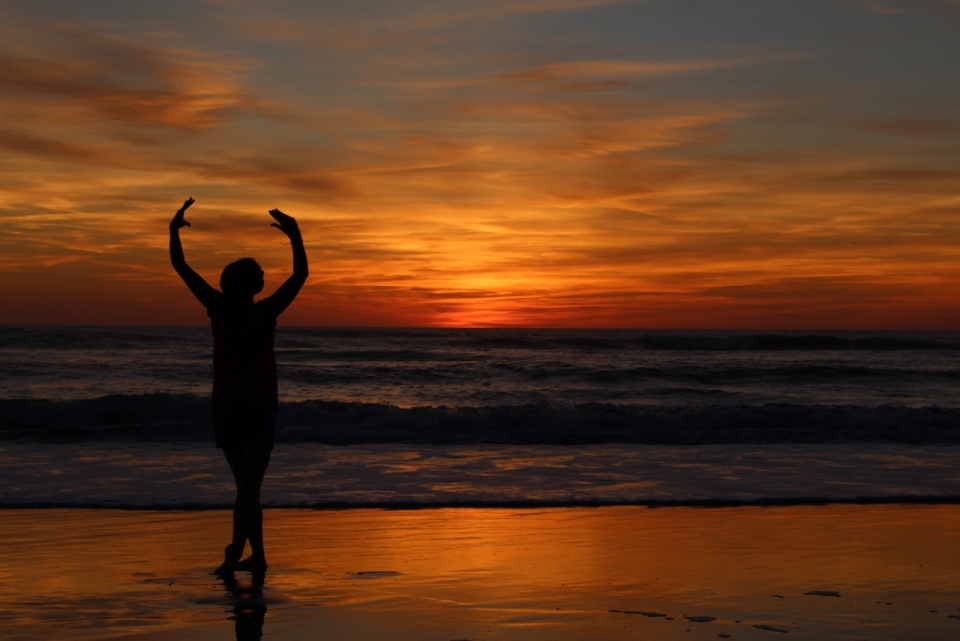 日落时分站在海滩上正在起舞的剪影