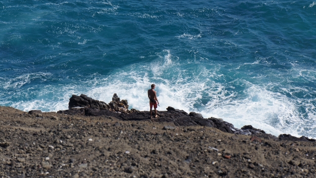悬崖边站立男性眺望翻滚海浪美景