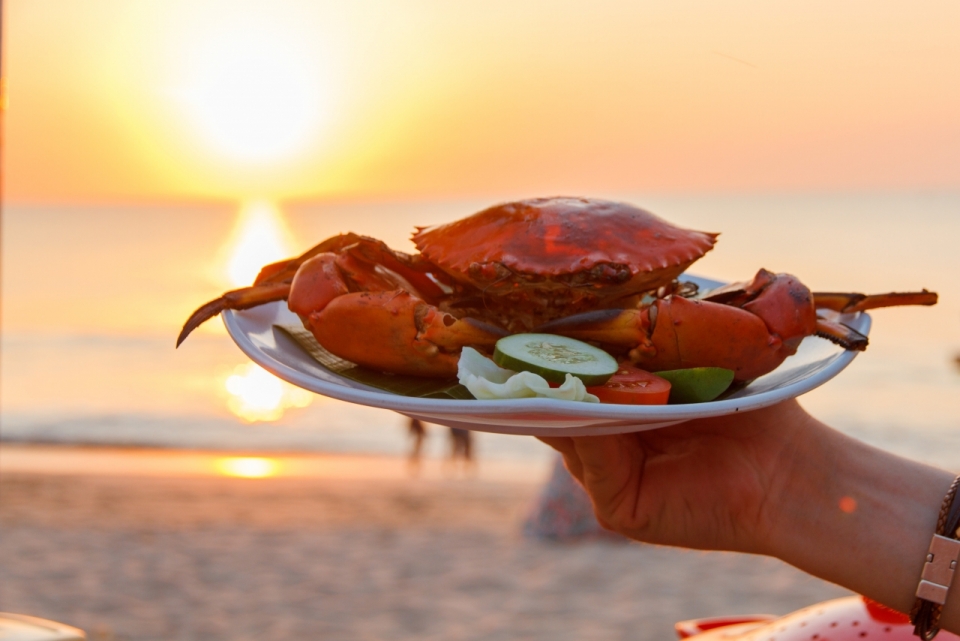 夕阳海滩边端着清蒸螃蟹手部和美食摄影