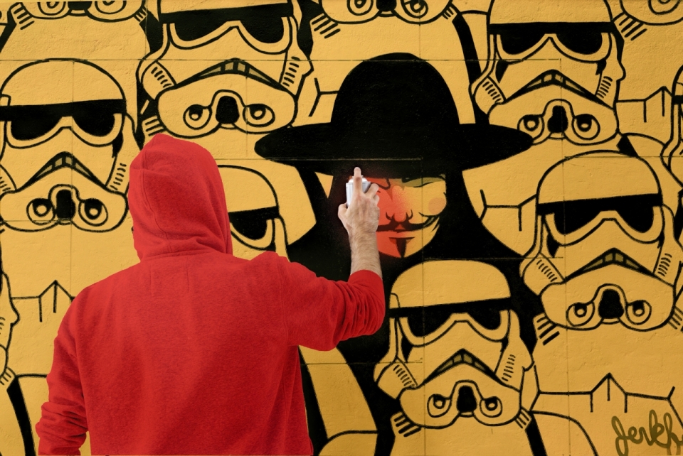 正在街头黄色墙壁上涂鸦的红色兜帽男子