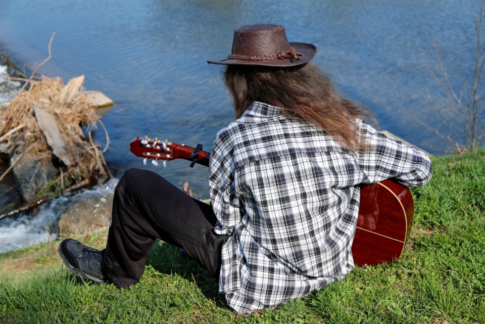 湖边坐在草坪上弹吉他的长发男子背影