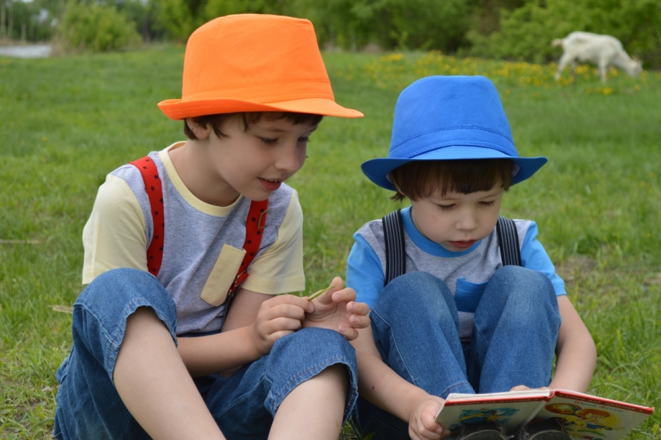 坐户外自然绿色草坪阅读书本戴彩色帽子男孩们