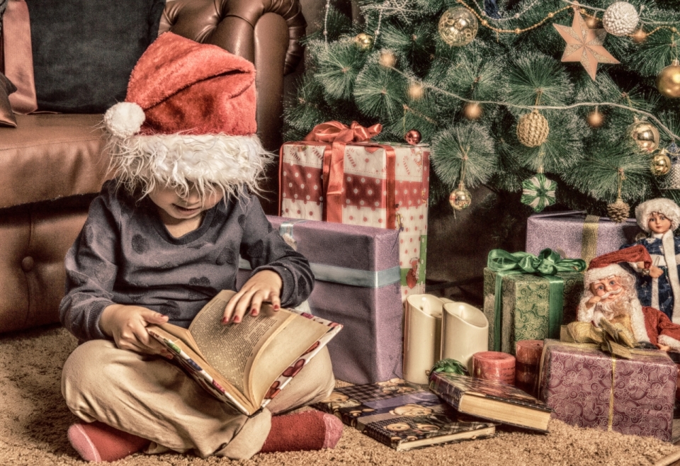 怀旧色调圣诞树装饰边戴圣诞帽阅读书本男孩