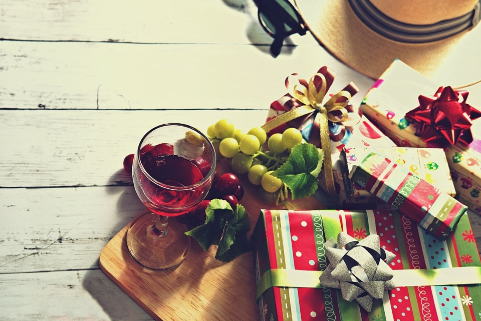 木桌上摆着眼镜帽子酒杯葡萄和包装各异的礼物盒