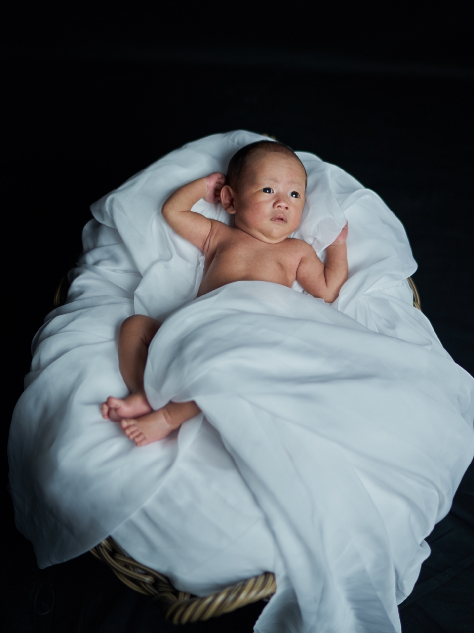 黑色背景上躺在垫着毯子木筐中的可爱婴儿
