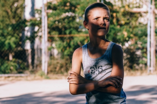 背景虚化阳光马路树荫下双手抱胸的男孩