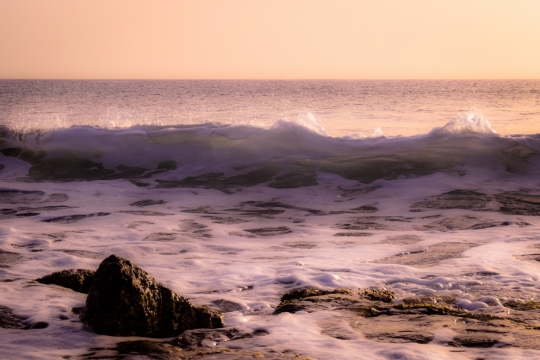 夕阳下大海波浪和沙滩边的礁石
