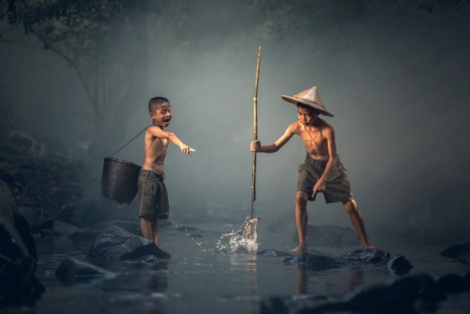 迷雾浓重的森林中两个小男孩在小溪里叉鱼