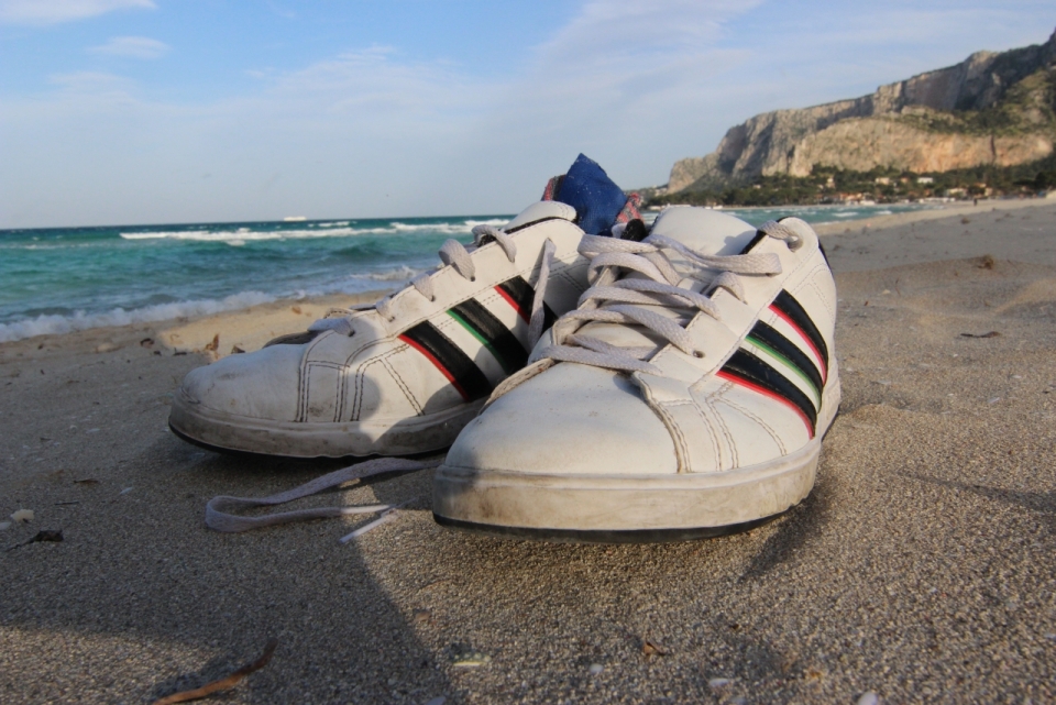 蓝色大海边的沙滩上放着一双白色板鞋