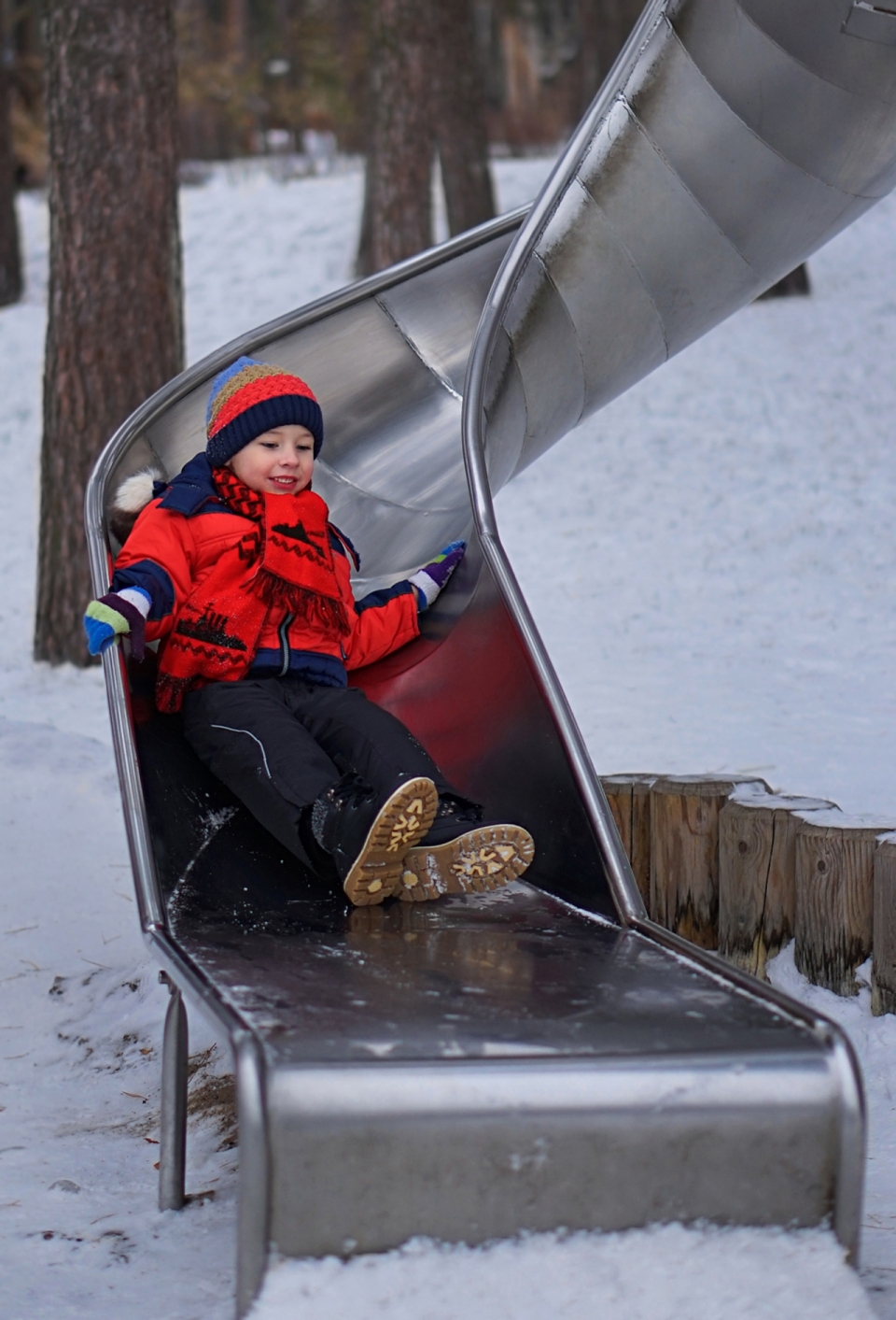 雪后自然公园金属滑梯游玩男孩