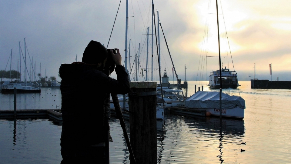 站在海边码头上摄影夕阳风光的男人
