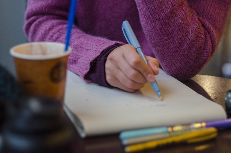 紫色毛衣女孩拿着笔在写字手边放着一杯咖啡