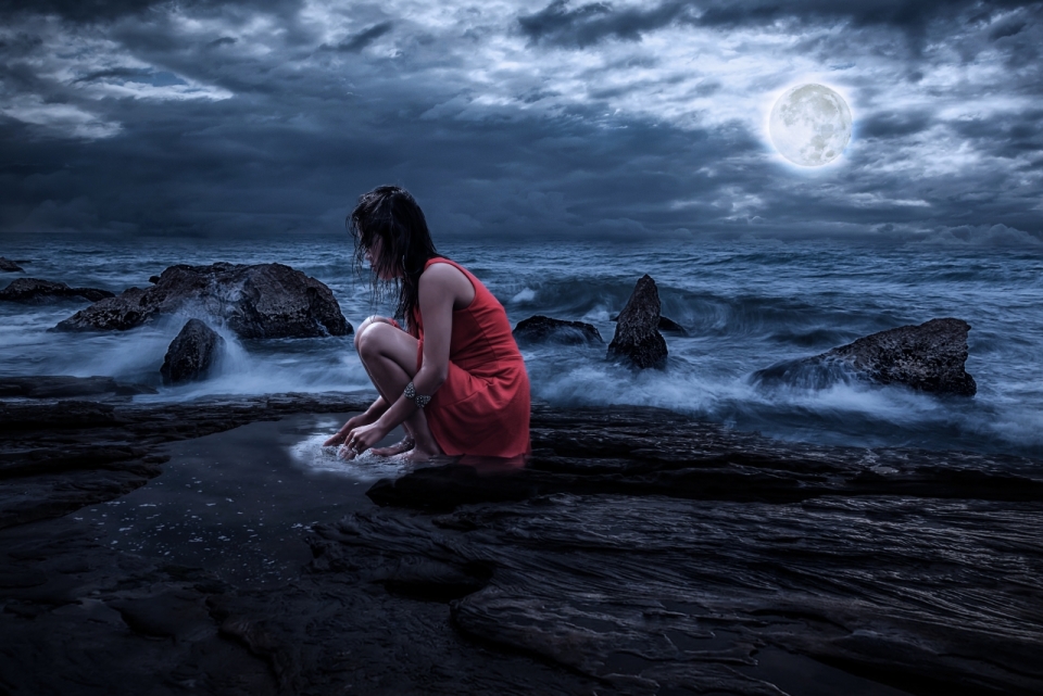 夜晚蹲坐在海边穿红衣服的女人