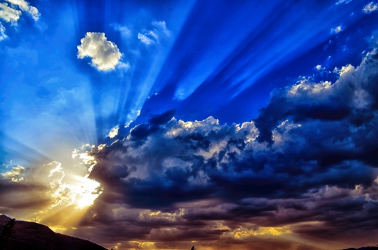 蓝天中白云后散发的太阳光芒