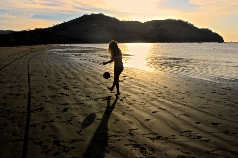 落日下的度假沙滩上女子踢球背影光影