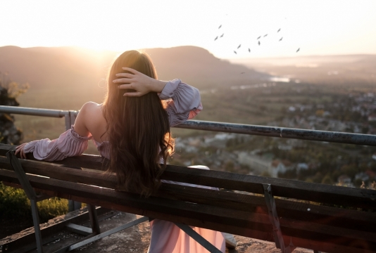 阳光下坐在小镇山坡长椅上的美女