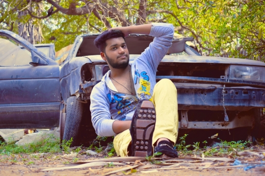 绿色树木靠坐在报废汽车前的男子