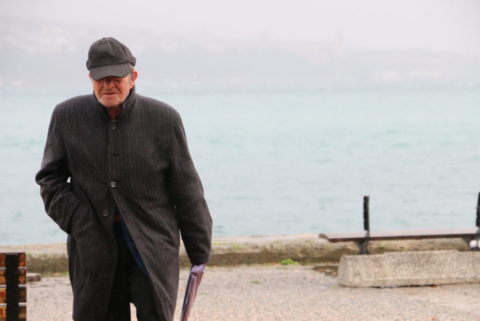 黑衣服戴帽子老爷爷在海边石桥上散步