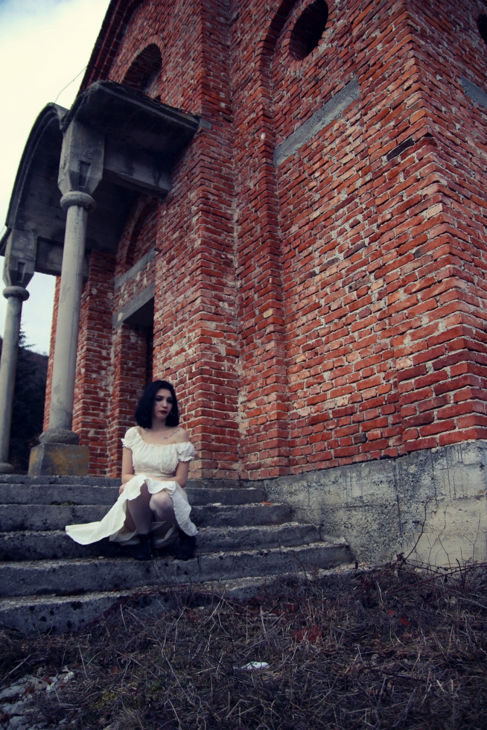老旧的红砖教堂门前坐在台阶上的白衣女子