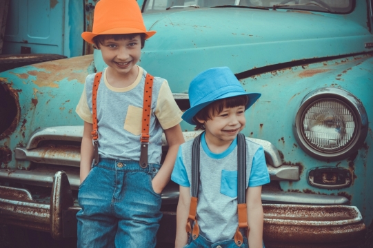 破旧废弃绿色轿车前戴帽子男孩们