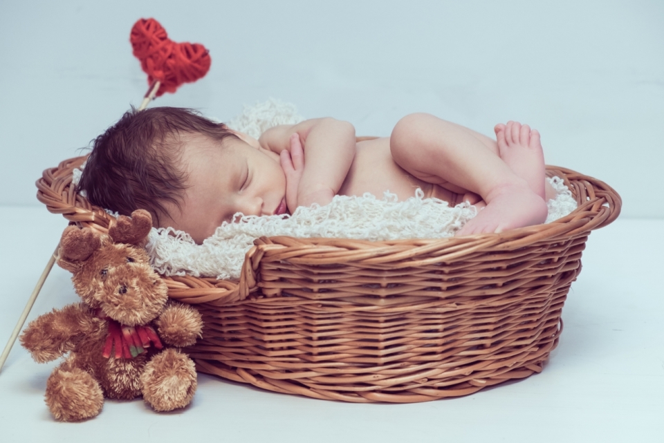 熟睡在木筐中毛毯上的婴儿和小熊玩偶