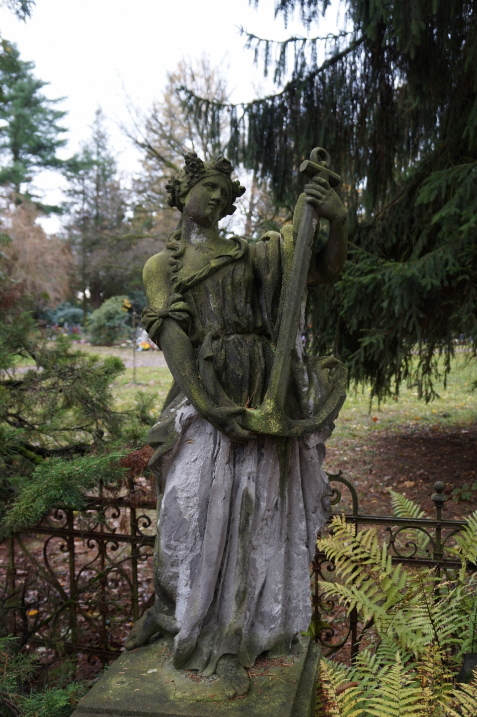 绿色树木围栏前抱着船锚的妇女雕像