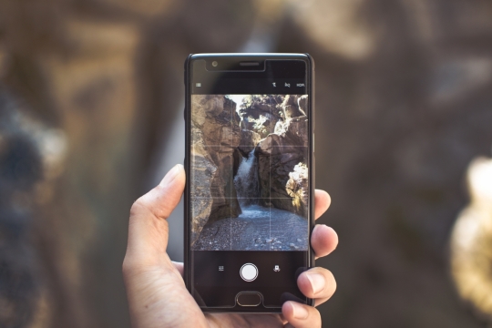 黑色智能手机拍摄阳光下自然瀑布风光