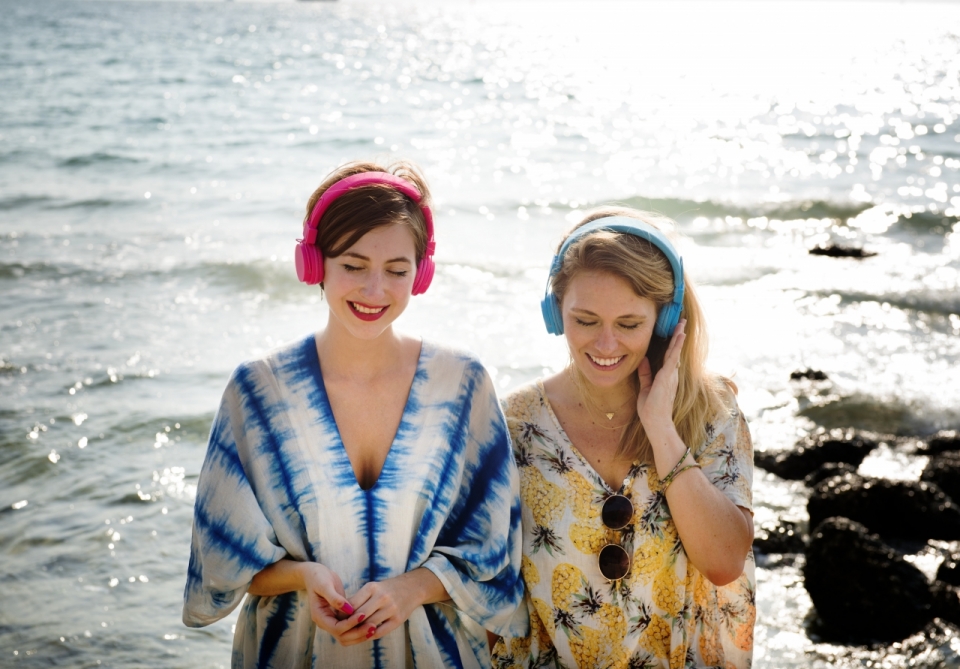 两个在大海边戴着耳机听音乐的美女
