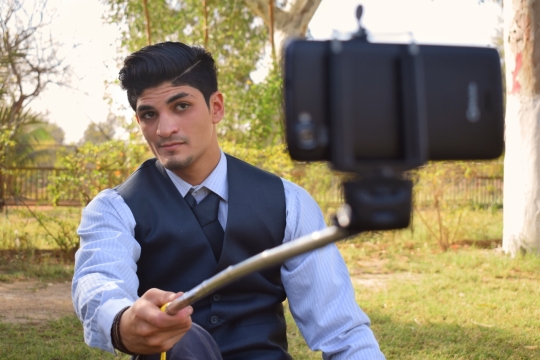 树荫下穿西装手拿自拍杆自拍的男子