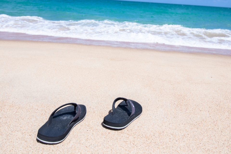 蓝色大海沙滩上两只黑色拖鞋摄影