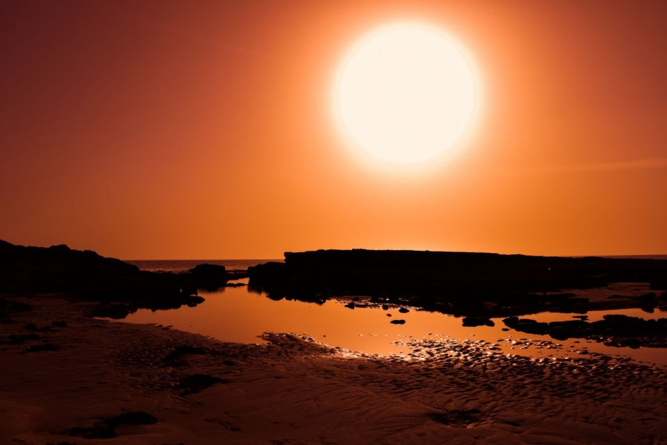 礁石海滩边红色落日摄影
