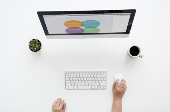 纯白办公桌上的电脑咖啡盆栽与正在办公的人