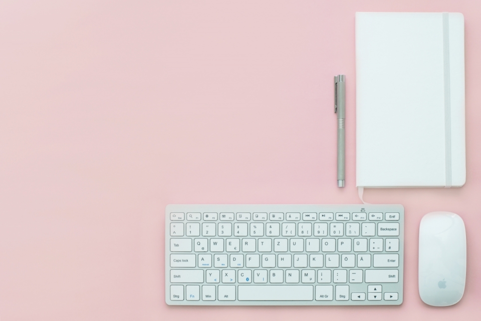 粉色桌子上的的键盘鼠标笔记本和钢笔