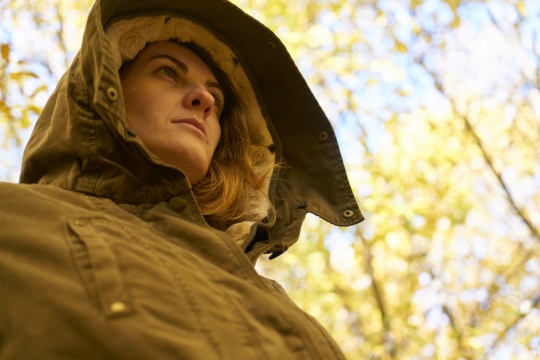 树林中穿着大衣带着兜帽看向远处的人