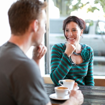 室内玻璃窗前摆咖啡木桌交谈的情侣