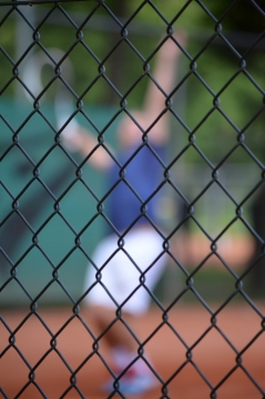 背景虚化的铁丝网后正在打网球的人