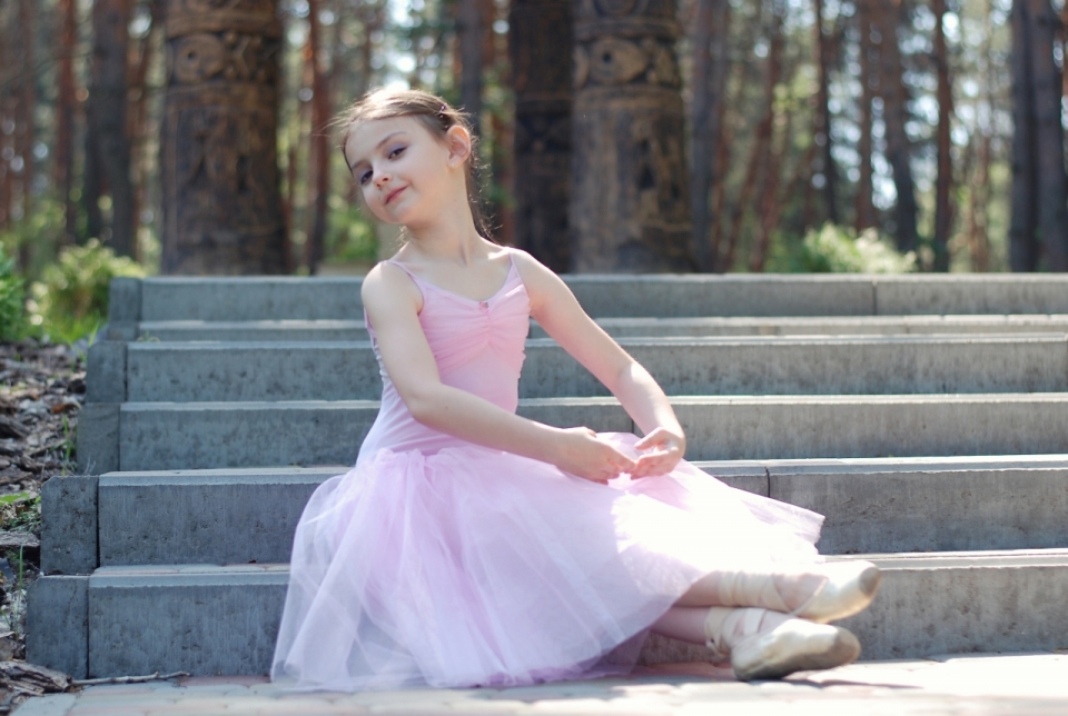 树林前坐在台阶上表演芭蕾的可爱女孩
