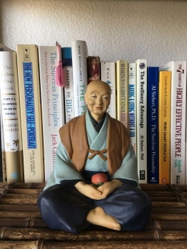 书架上盘坐拿着苹果的老人玩偶摆设