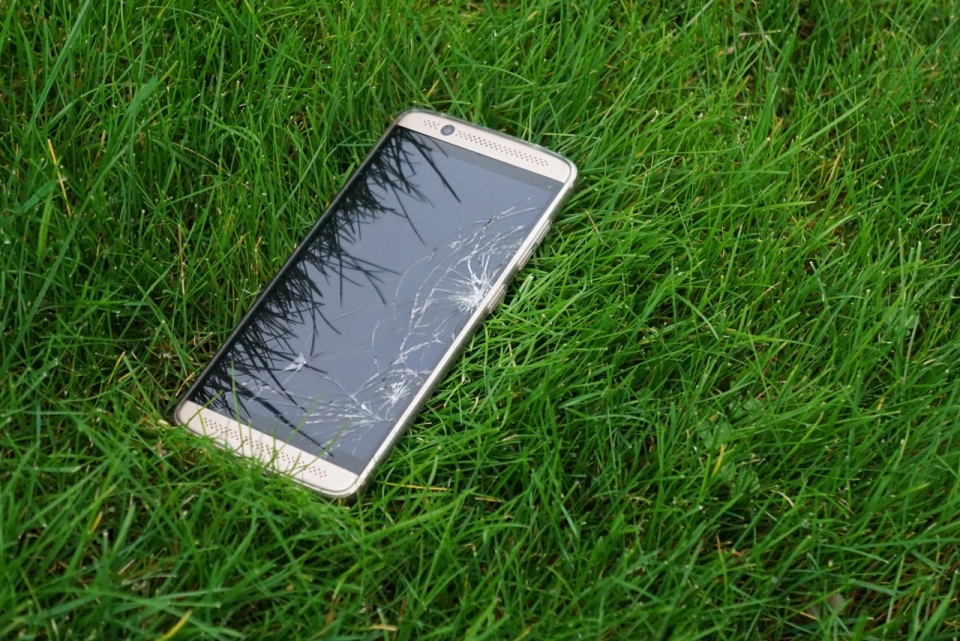 掉在翠绿草坪上的屏幕碎裂的手机