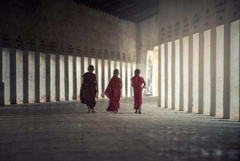 三个小男孩穿着红色僧袍走在宽敞的场地上