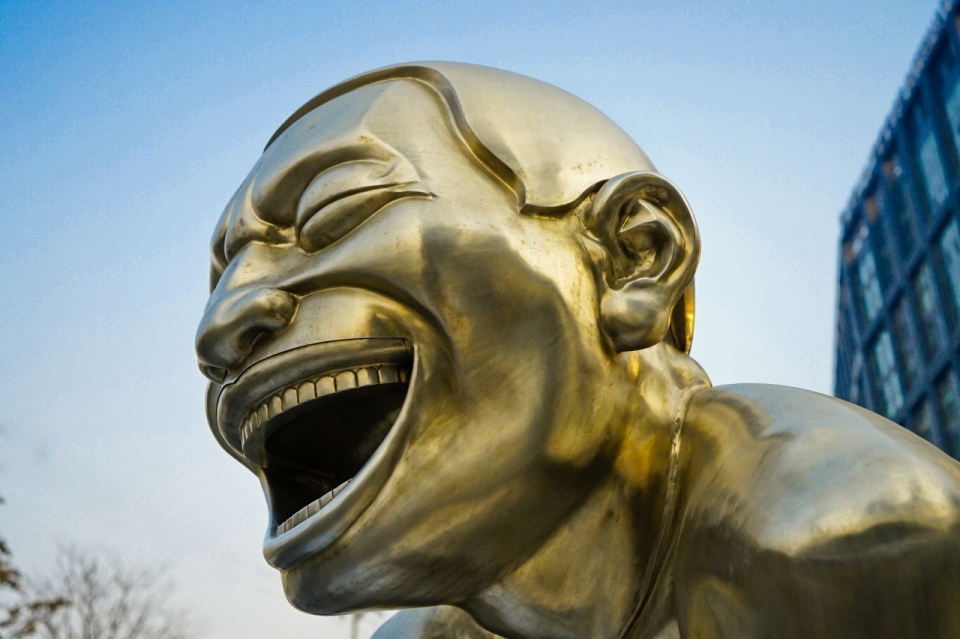 蓝天下城市街道边金色大笑雕像脸部摄影