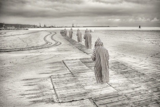 沙滩栈道上穿着斗篷排列行走的人